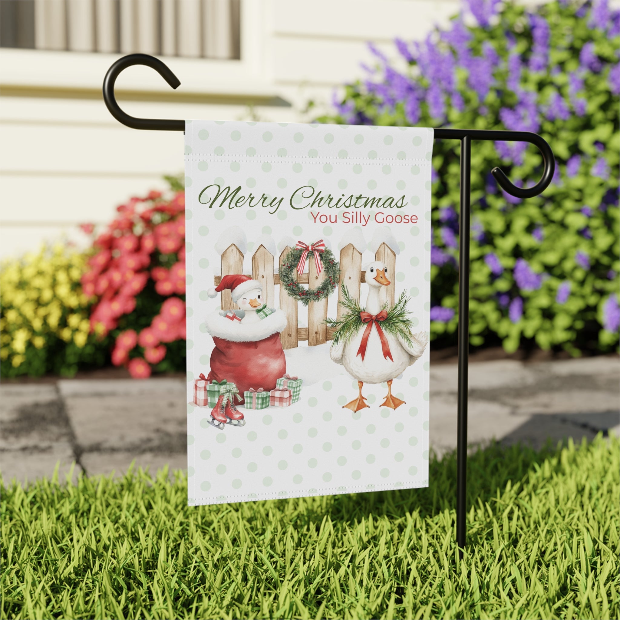 Christmas-themed garden flag with cartoon characters on a stand in front of flowers