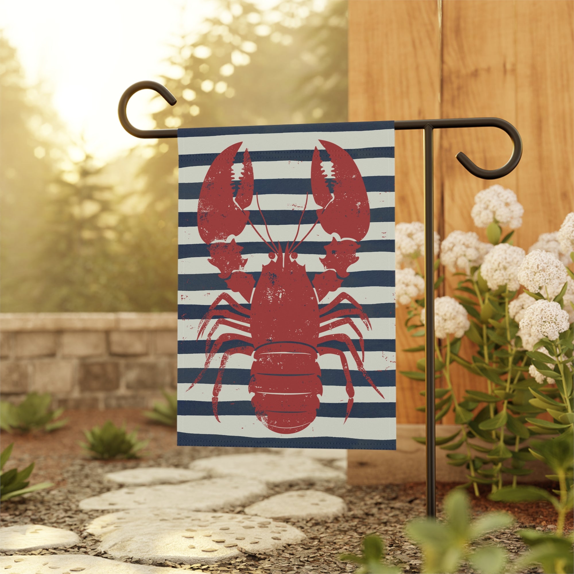 Decorative garden flag with a red lobster design on a blue and white striped background, hanging outdoors.