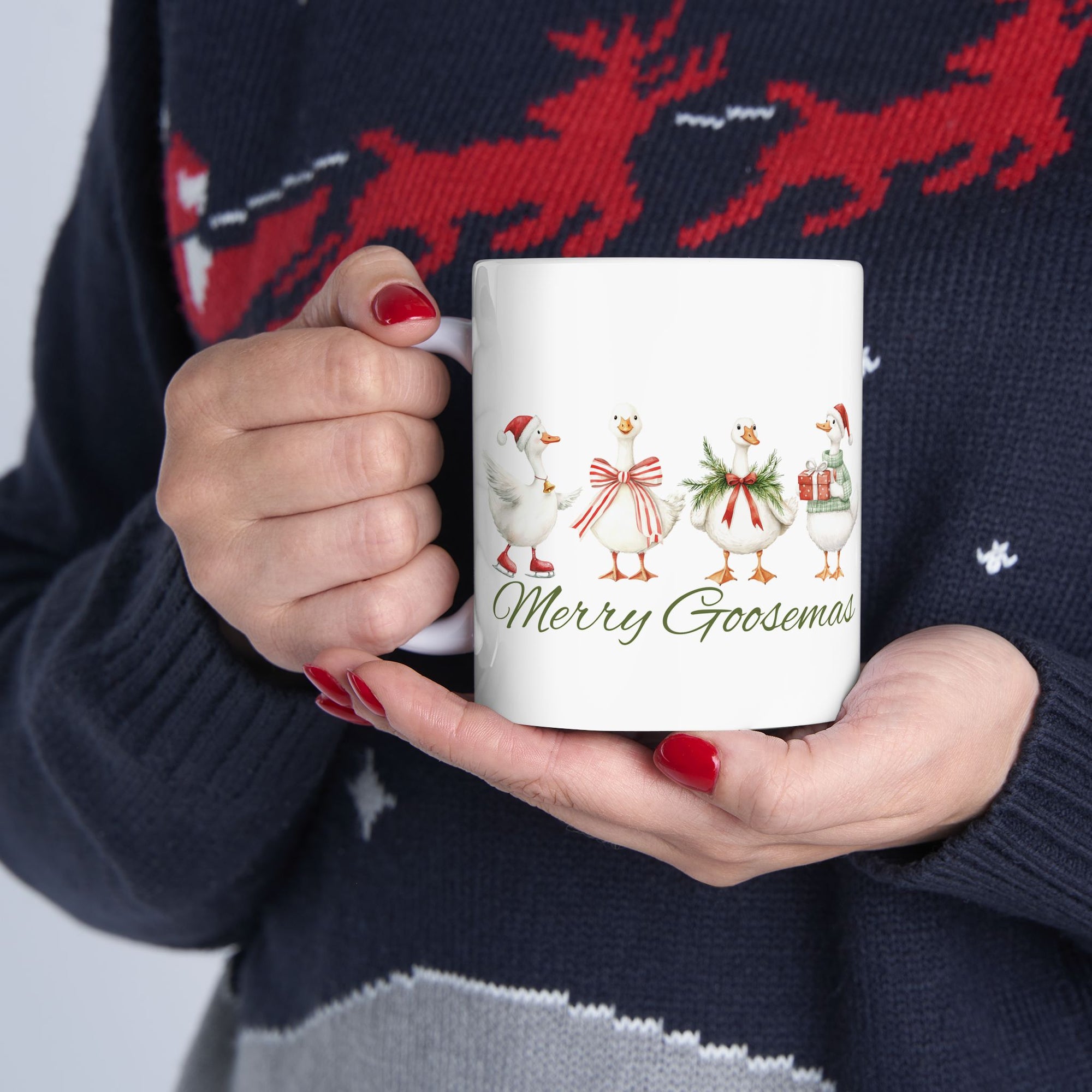 Person holding a mug with 'Merry Goosemas' design, wearing a festive sweater with reindeer.