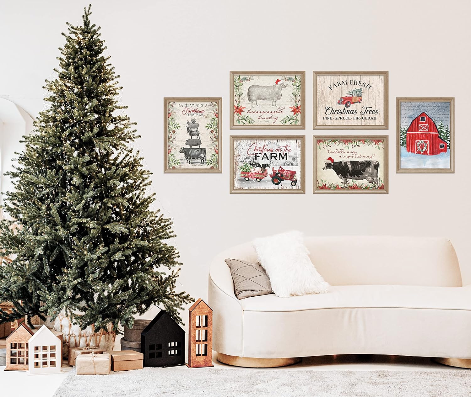 A collection of framed Christmas-themed prints with vintage Santa and reindeer imagery displayed above a white sofa, beside a decorated Christmas tree and miniature houses.