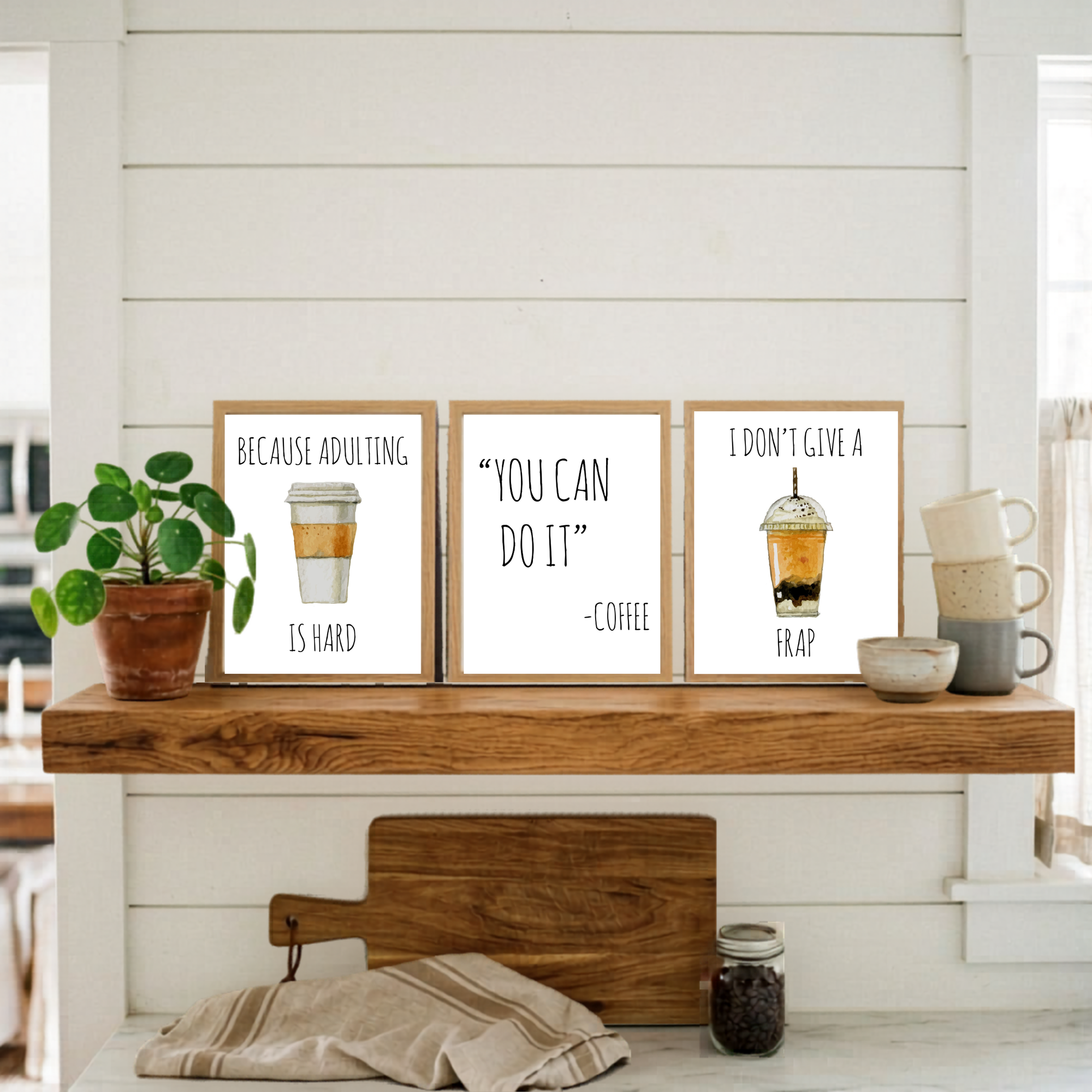 Three framed prints on a wooden shelf with a plant and kitchen items.