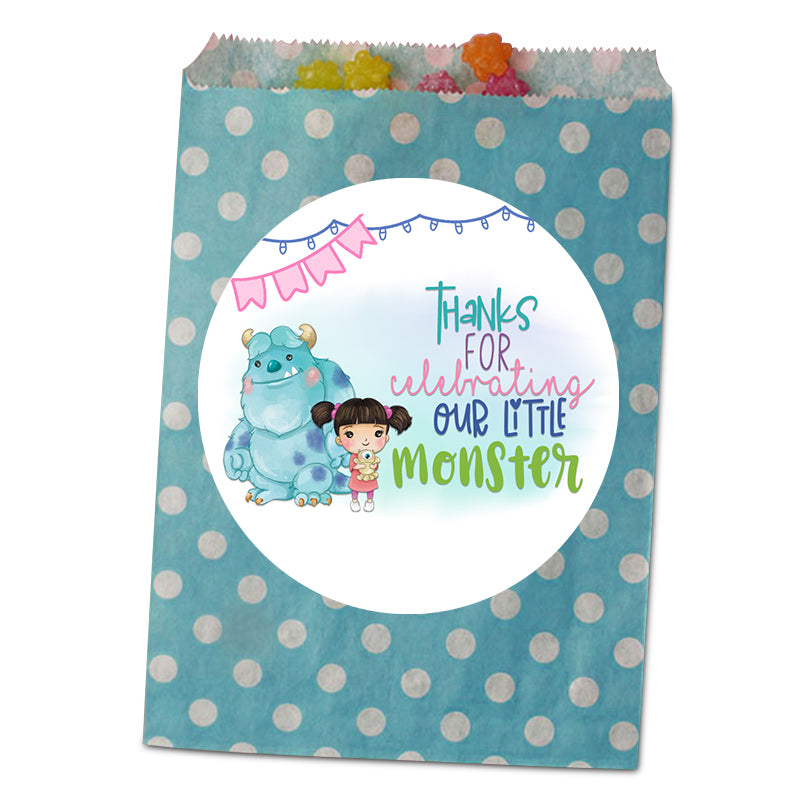 A teal paper party favor bag with white polka dots and a large white oval sticker on the front. The sticker features a cartoon monster and the text 'THANKS FOR celebrating OUR LITTLE MONSTER' in colorful lettering.